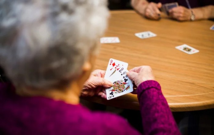 An elderly person playing a card game at a table.
