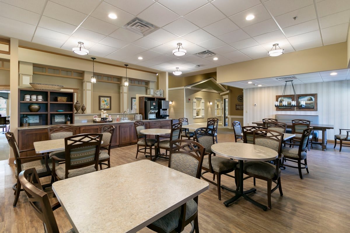 A cozy dining area with neatly arranged tables and chairs, illuminated by warm lighting.