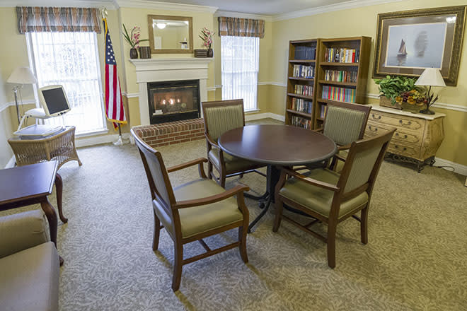A cozy living room with a fireplace, round table and chairs, and a bookshelf by the window.