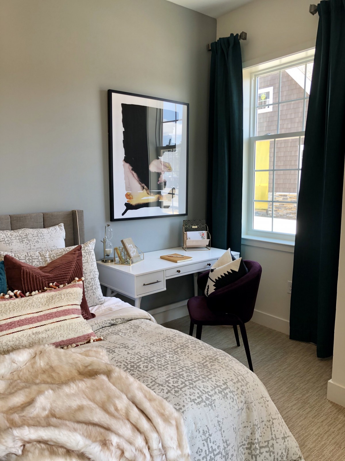 A cozy bedroom with a stylish desk beside the window, complemented by modern decor and artwork.