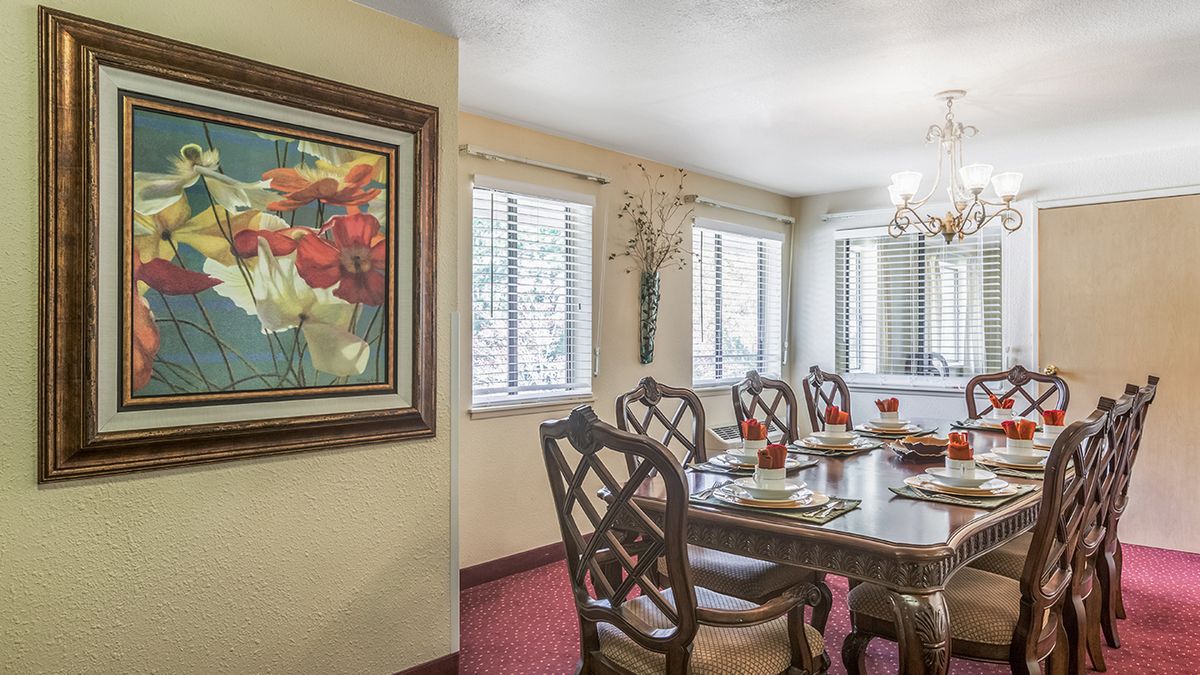 A well-decorated dining room featuring a wooden dining table with chairs, a chandelier, and a colorful painting on the wall.