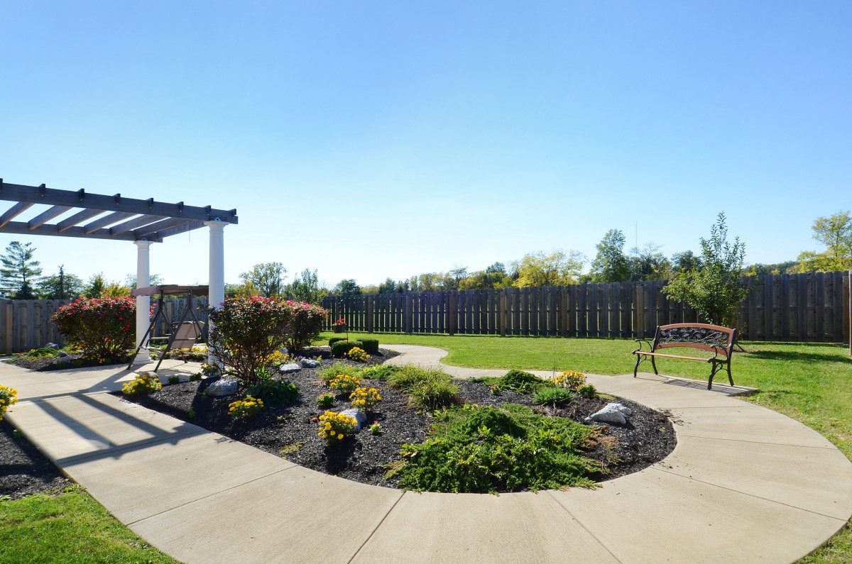 A neatly landscaped garden with a variety of plants, a well-maintained lawn, and paved walkways under a clear blue sky.