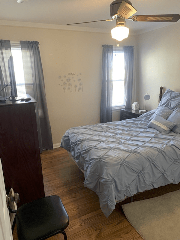A cozy bedroom with a neatly made bed, two windows with curtains, and a chest of drawers.