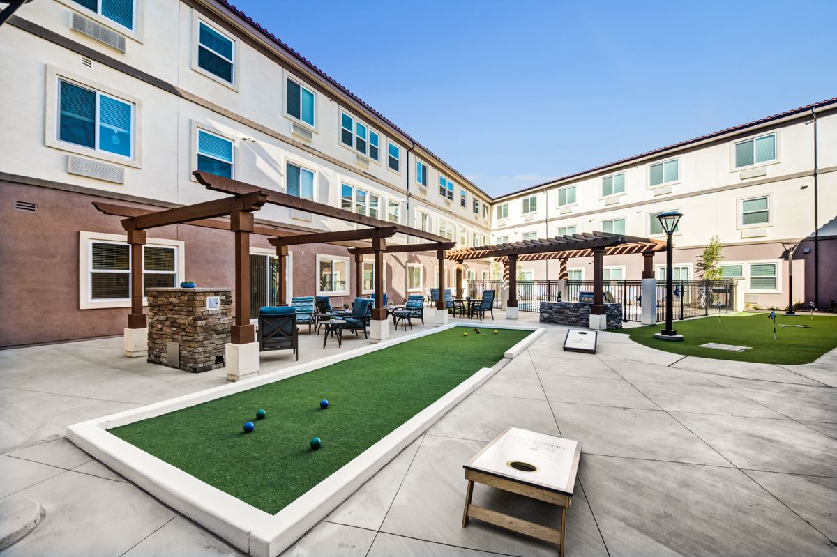 A modern apartment courtyard featuring seating areas, pergolas, and a bocce court.
