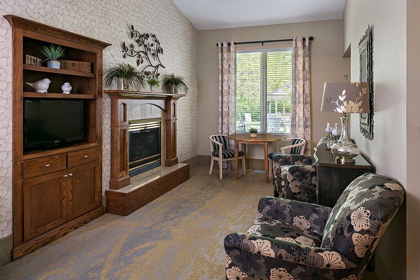 A cozy living room featuring a fireplace, television, and floral-patterned chairs.