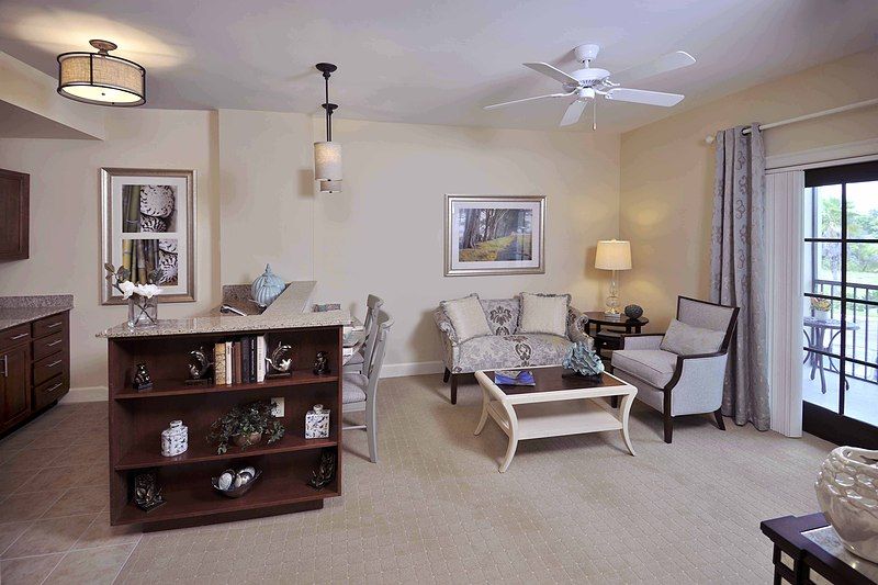 A cozy living room with a sofa, coffee table, and bookshelf, decorated with artwork and a lamp.