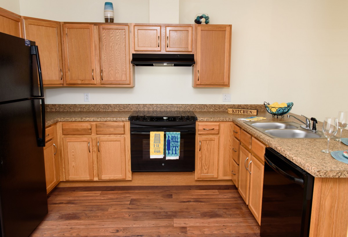 A modern kitchen with wooden cabinets and flooring, featuring a black stove and sink.