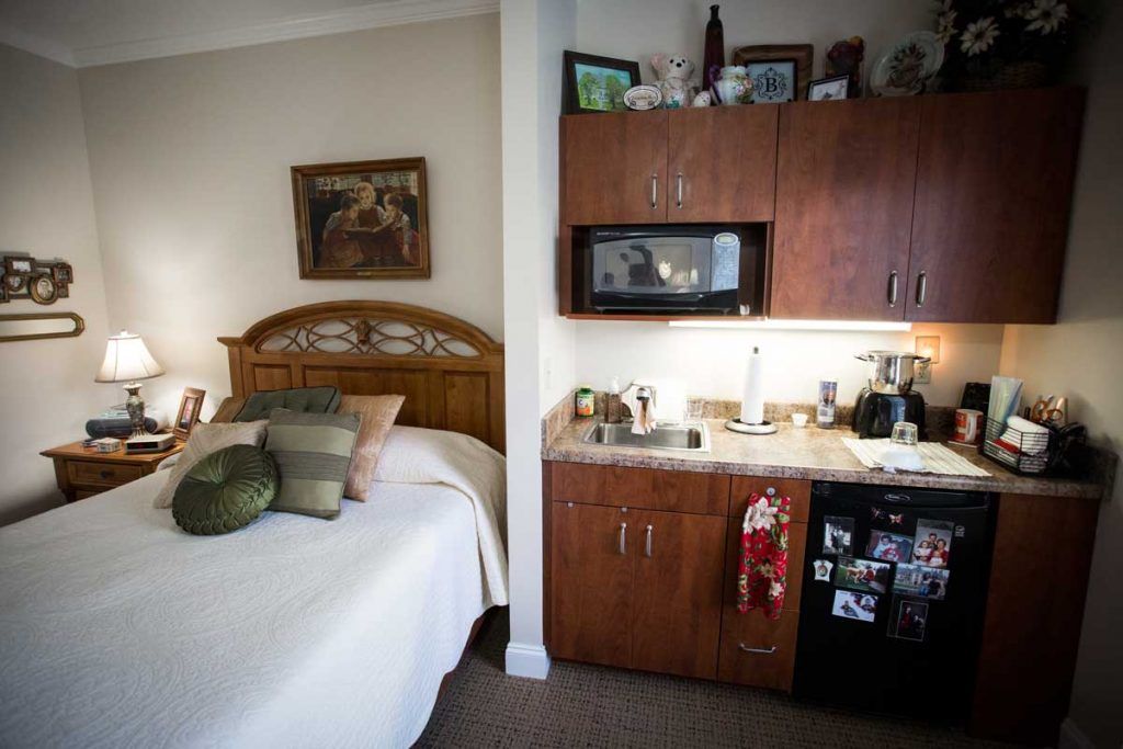 A cozy studio apartment with a bed and a small kitchenette featuring a microwave and mini-fridge.