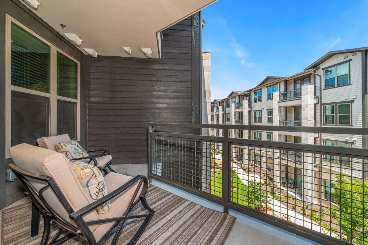 A modern apartment balcony with comfortable seating overlooking a residential complex.