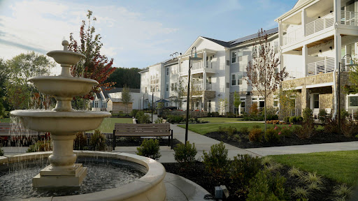 A serene view of a modern apartment complex featuring landscaped gardens and a decorative fountain.