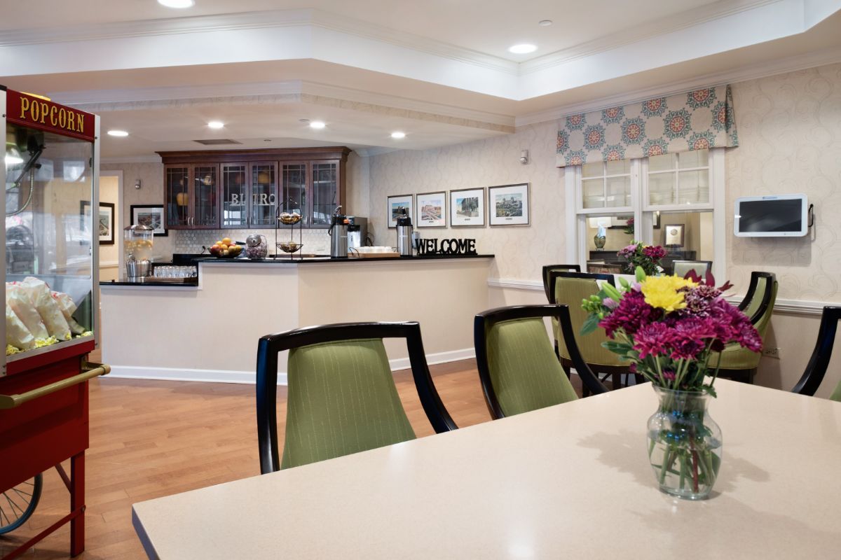 A modern dining area with a kitchenette, featuring green chairs and a table with a flower arrangement.
