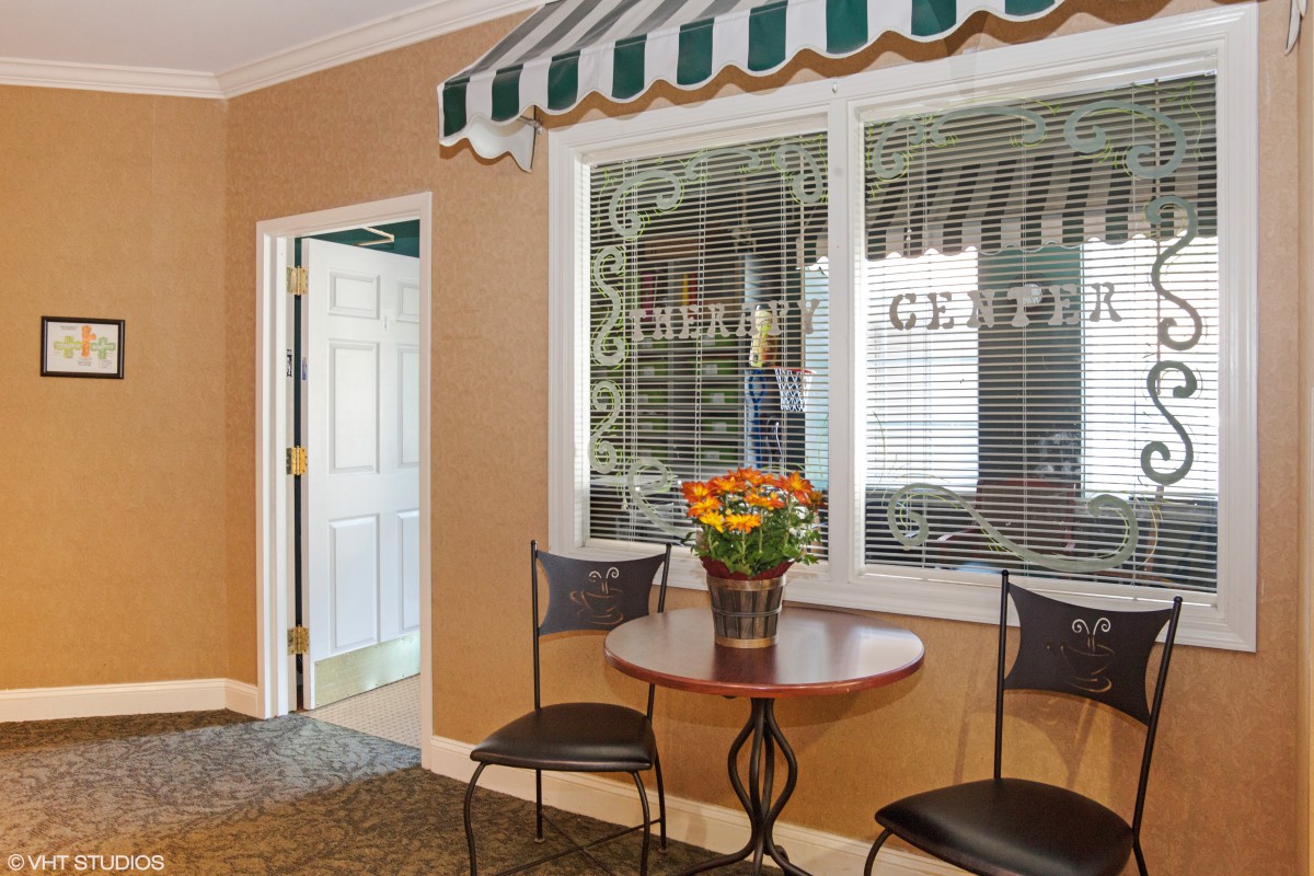 A cozy indoor seating area with a small round table, two chairs, and a pot of flowers under an awning.