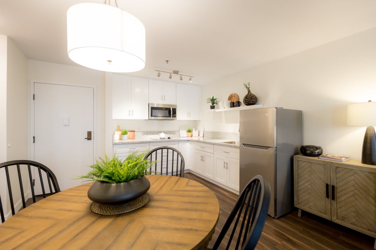 A modern kitchen with a dining area featuring a round wooden table and contemporary lighting.