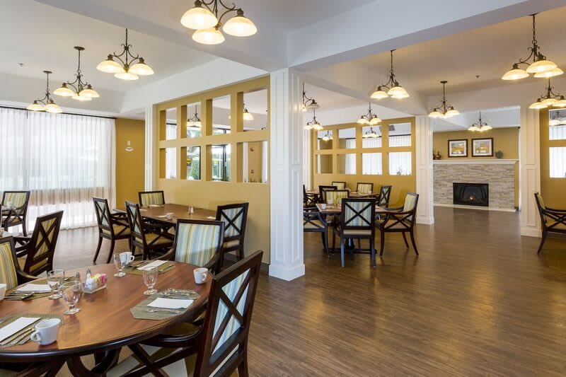 A spacious dining area with wooden tables and chairs, well-lit by elegant lighting fixtures.