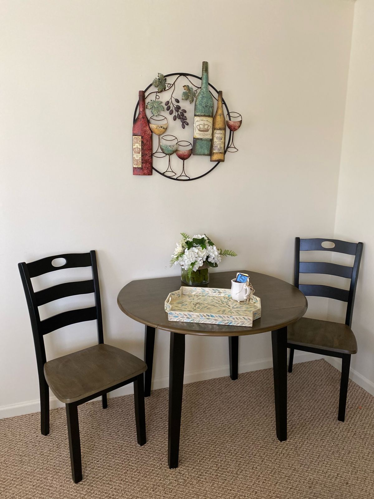 A small dining setup with a round table, two chairs, and wall art.