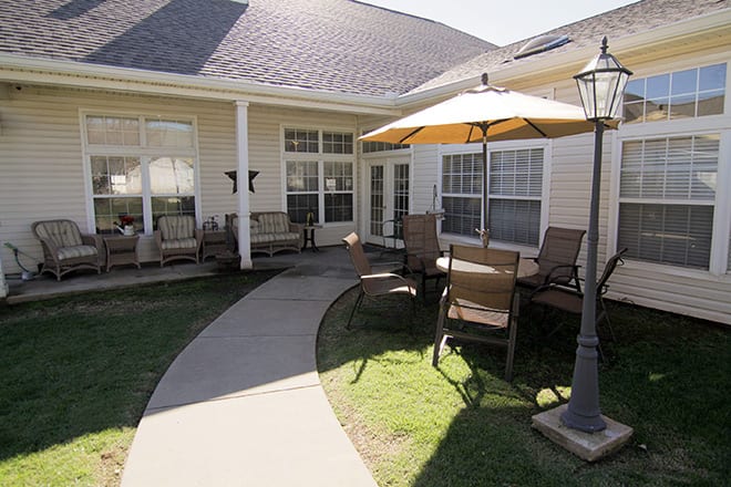 A cozy outdoor patio area with chairs and a large umbrella, connected by a paved pathway to the house.