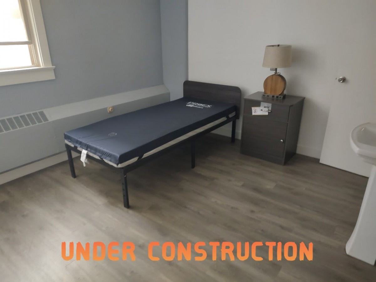 Minimalist bedroom with a single bed and nightstand, labeled 'Under Construction'.