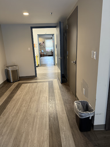 A modern office hallway featuring wooden flooring and a trash can.