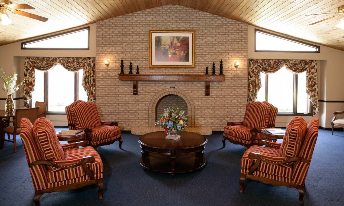 A cozy living room with a brick fireplace, surrounded by striped armchairs and a wooden coffee table.