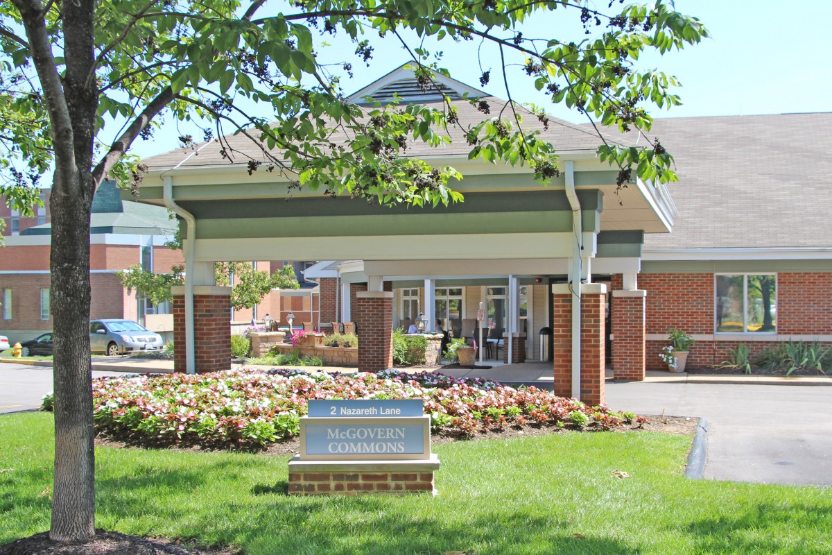 A welcoming building entrance with an awning and well-maintained landscaping featuring flowers and a tree.