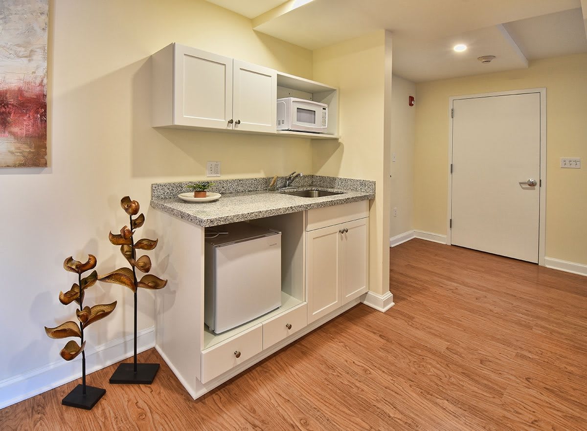 A compact kitchenette with cabinets, a microwave, mini fridge, and sink set against wood flooring.