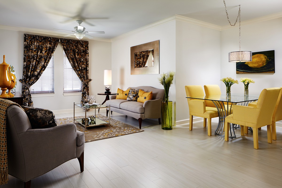 A modern living and dining space featuring a gray sofa, yellow dining chairs, decorative plants, and contemporary decor.