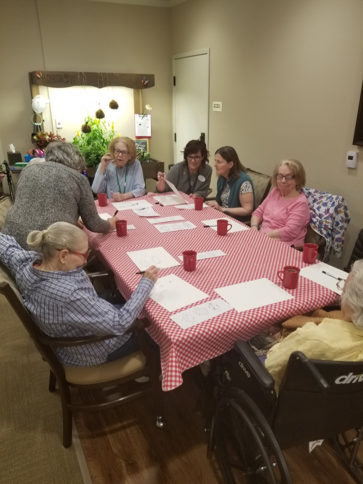 A group of seniors engaged in an indoor activity around a table.