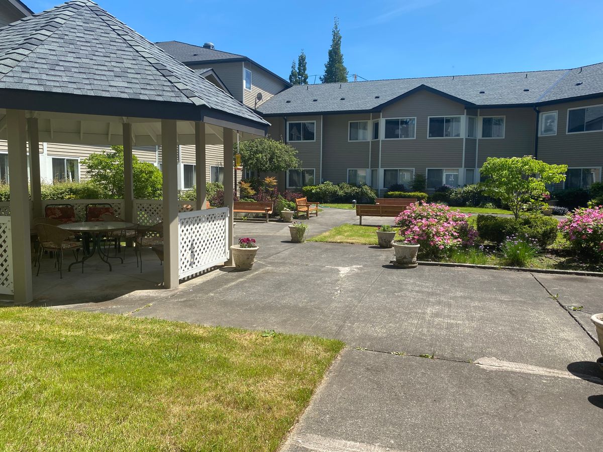 A view of a landscaped garden with a gazebo and a residential building in the background.