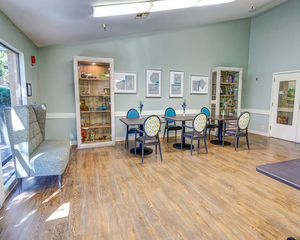 A cozy room with tables, chairs, bookshelves, and artwork on the walls.