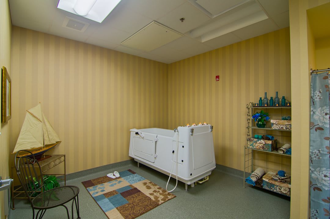 A bathroom with a specialized bathtub and shelves stocked with towels, featuring striped wallpaper and bright lighting.