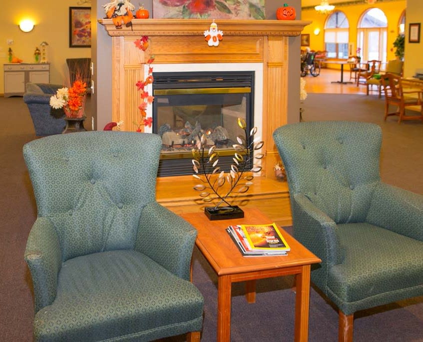 A cozy living room with two chairs facing a fireplace and a small coffee table.