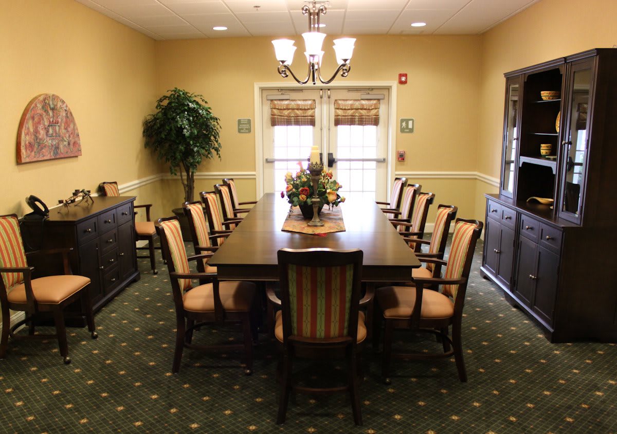 A well-lit dining room with a long table and elegant chairs, adorned with a central floral arrangement.