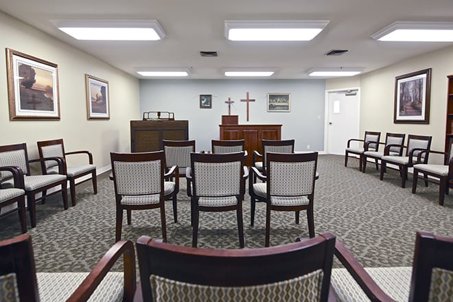 A small chapel room with arranged seating and a cross at the front.