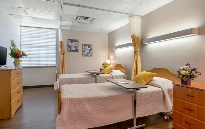 A hospital room with twin beds, separated by curtains and equipped with bedside tables.