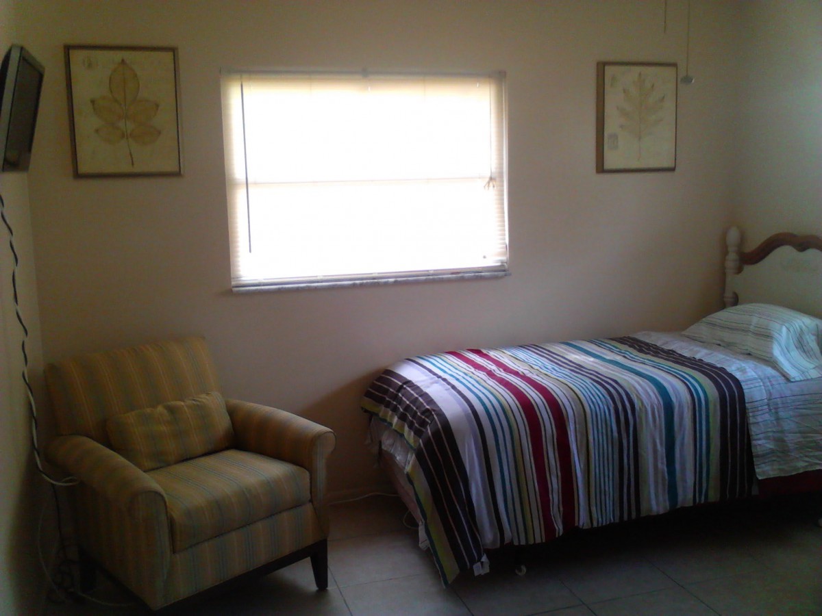 A cozy bedroom featuring a single bed with a striped blanket and an armchair by the window.