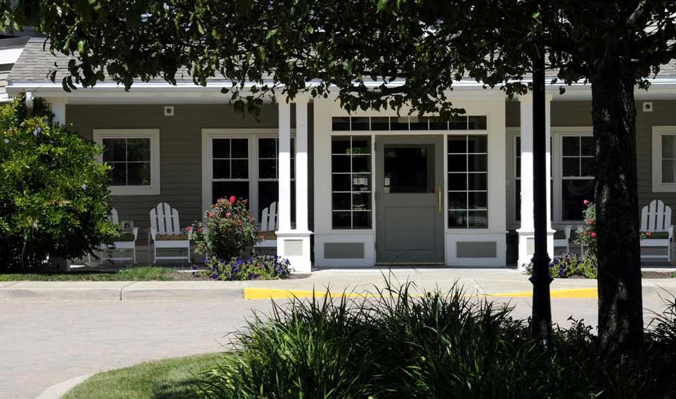 A quaint house with a porch and chairs surrounded by greenery.