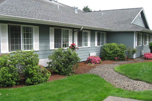 A well-maintained front yard with a green lawn and neatly arranged shrubs in front of a house.