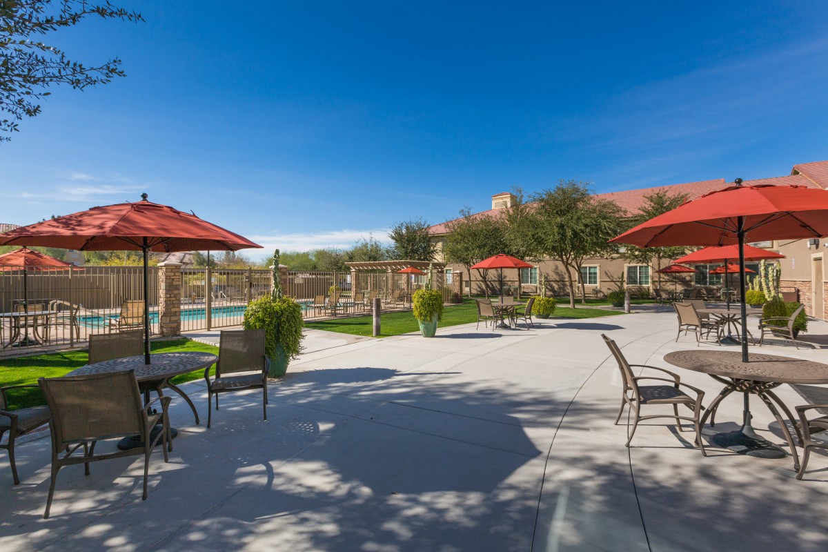A sunny outdoor patio area with tables, chairs, umbrellas and a nearby pool.