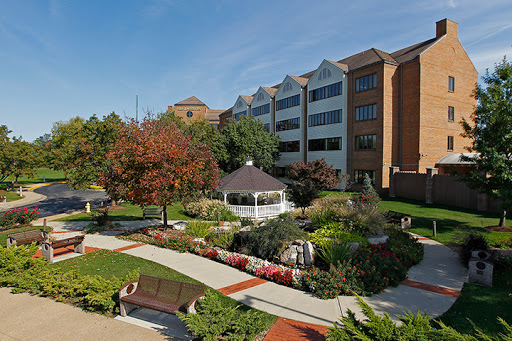 A serene garden area featuring a gazebo, surrounded by colorful flowers and modern buildings.