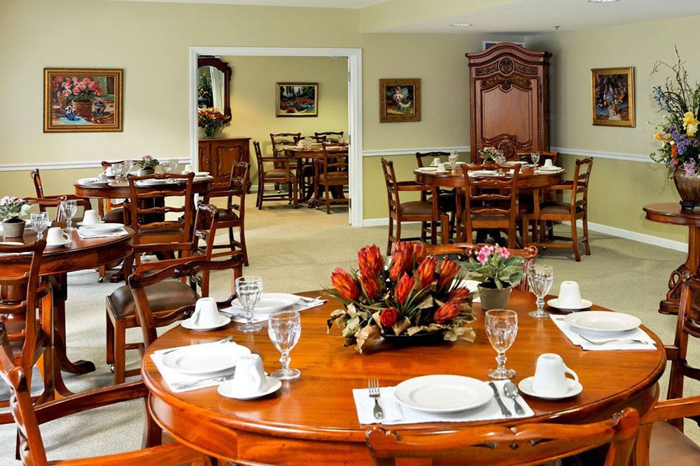 An elegantly set dining room with polished wooden tables and floral arrangements.