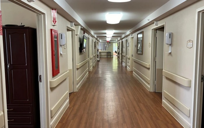 A long, well-lit corridor with wooden flooring and multiple doors.