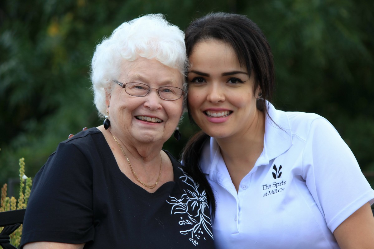 An elderly woman and a young woman smiling together outdoors.