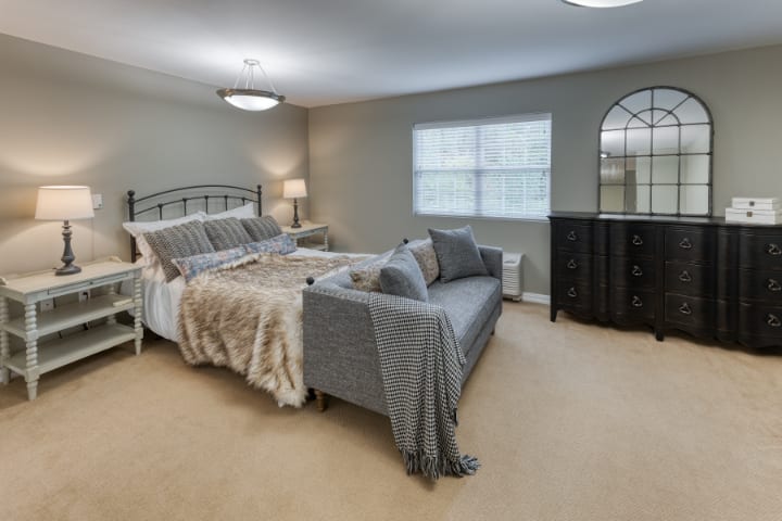 A spacious bedroom with a large bed, a sofa at the foot of the bed, and a dresser by the window.