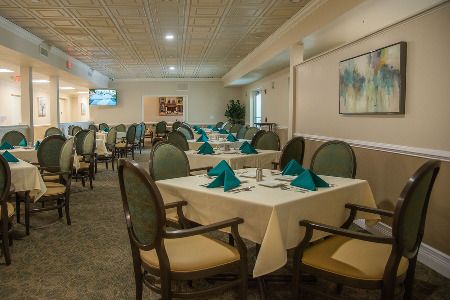 An elegantly arranged dining area with neatly set tables and chairs, featuring teal napkins and framed artwork on the walls.