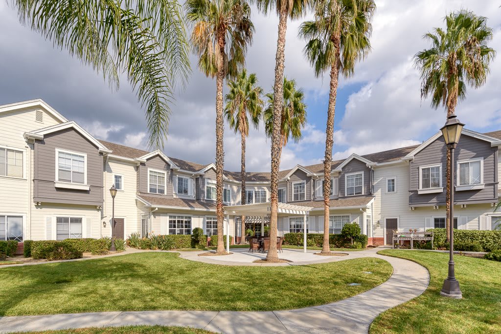 A two-story residential building surrounded by palm trees and a paved pathway under a partly cloudy sky.
