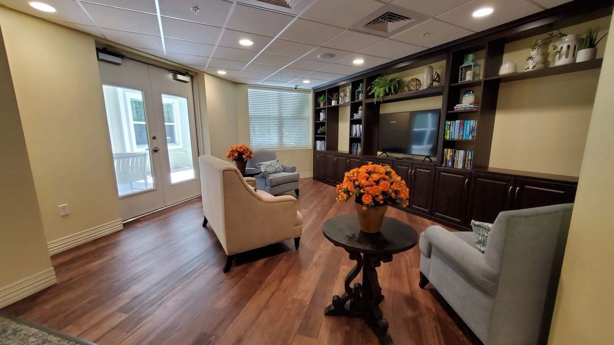 A cozy living room with elegant furniture, wood flooring, and decorative bookshelves adorned with potted plants.