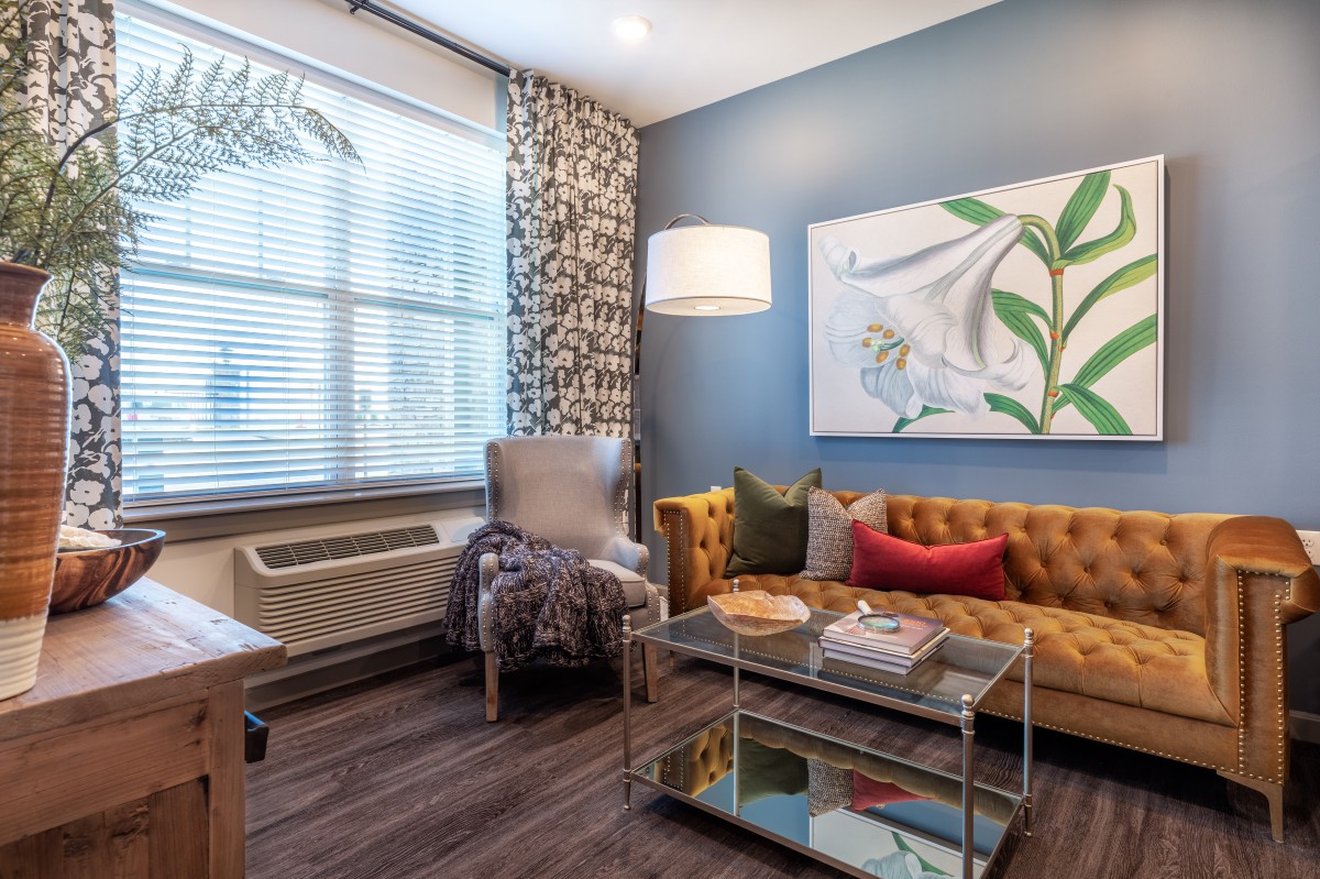 A cozy living room with modern decor, featuring a tufted sofa, a glass coffee table, and large artwork on the wall.