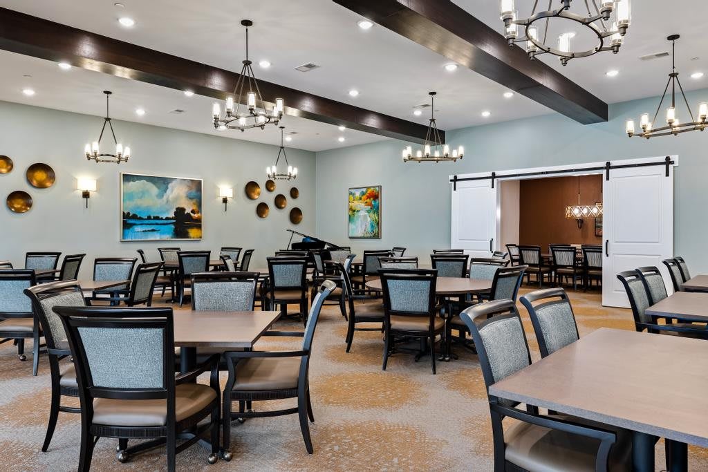 A modern dining room featuring elegantly arranged tables and chairs, adorned with chandeliers and contemporary artwork.