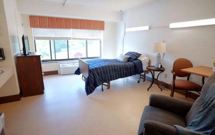 A spacious bedroom with a large window, bed, and comfortable seating area.