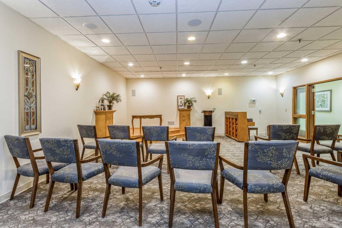 A spacious meeting room with rows of chairs facing a wooden stand and piano.